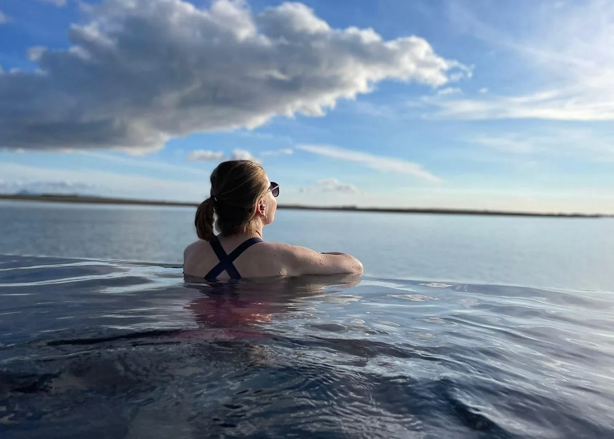 A woman in the infinity pool seen from behind, looking out at the sea and the sky