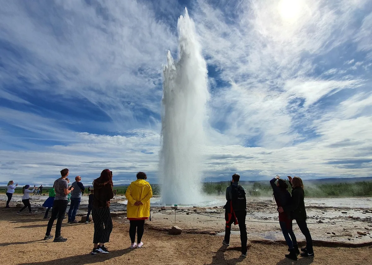 Une foule regardant le geyser Strokkur entrer en éruption sous un ciel lumineux